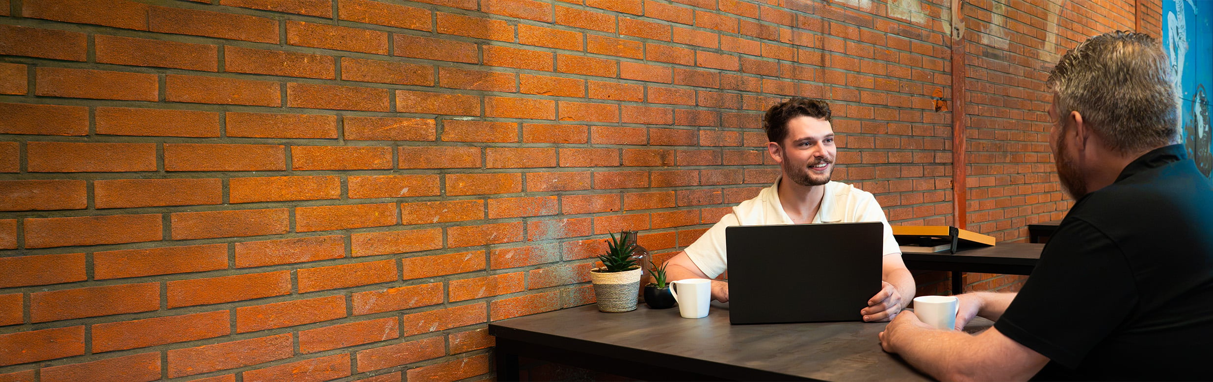 Medewerker van KlokGroep in gesprek met accountmanager van Azerty aan tafel met laptop en koffie