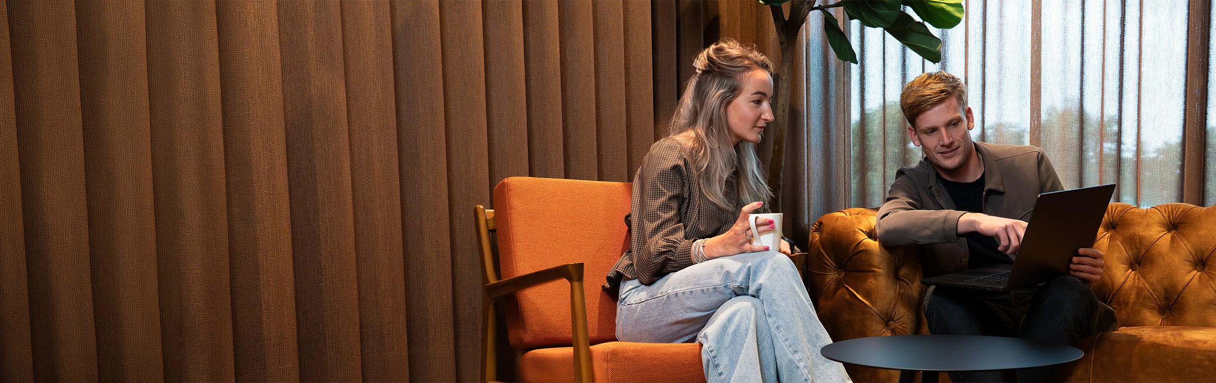 Twee collega's overleggen met laptop en koffie in een sfeervolle lounge