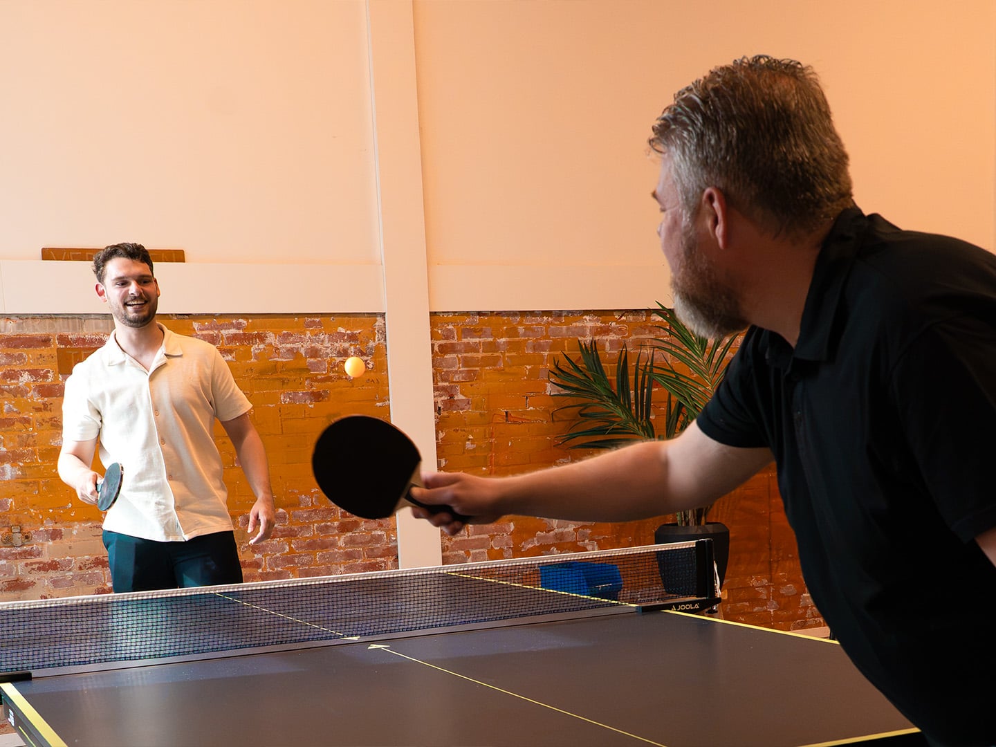 Twee Azerty-collega's spelen lachend een potje tafeltennis op kantoor